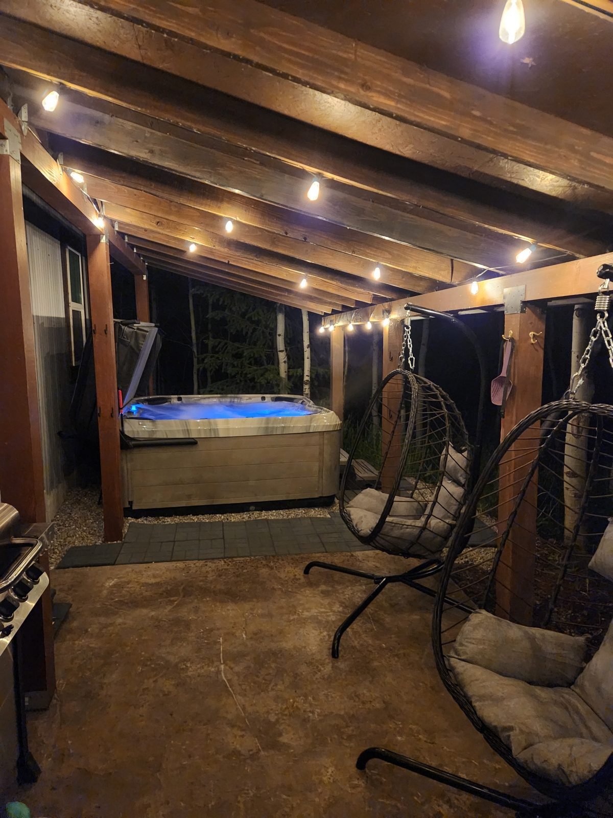 Covered spa lounge with hot tub and string lights at dusk
